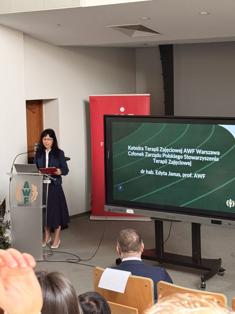 dr hab. Edyta Janus prof. AWF, na uroczystym rozpoczęciu konferencji, ubrana w granatową sukienkę, ma na sobie okulary, ma czarne włosy